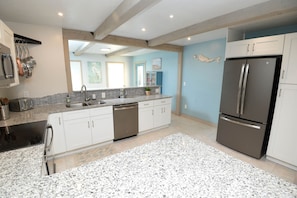 A modern kitchen with white cabinets, a granite countertop, stainless steel appliances, and a light blue accent wall.