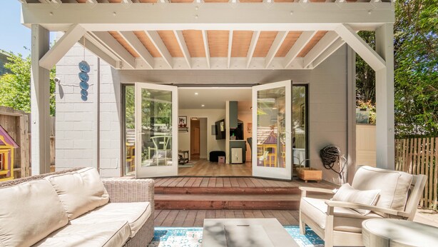 Un patio ouvert avec un espace salon couvert, une terrasse en bois et une vue sur l’intérieur de la maison.