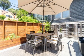 Un patio al aire libre con mesa y sillas de madera, un paraguas grande y una cerca de madera.