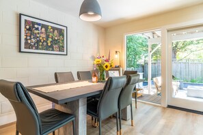 Un comedor con una mesa, sillas, un jarrón de flores y un cuadro en la pared.
