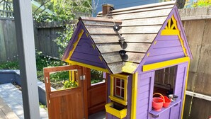 Une petite maison de jeu en bois, aux couleurs violettes et jaunes, dotée d’une fenêtre et d’une porte.