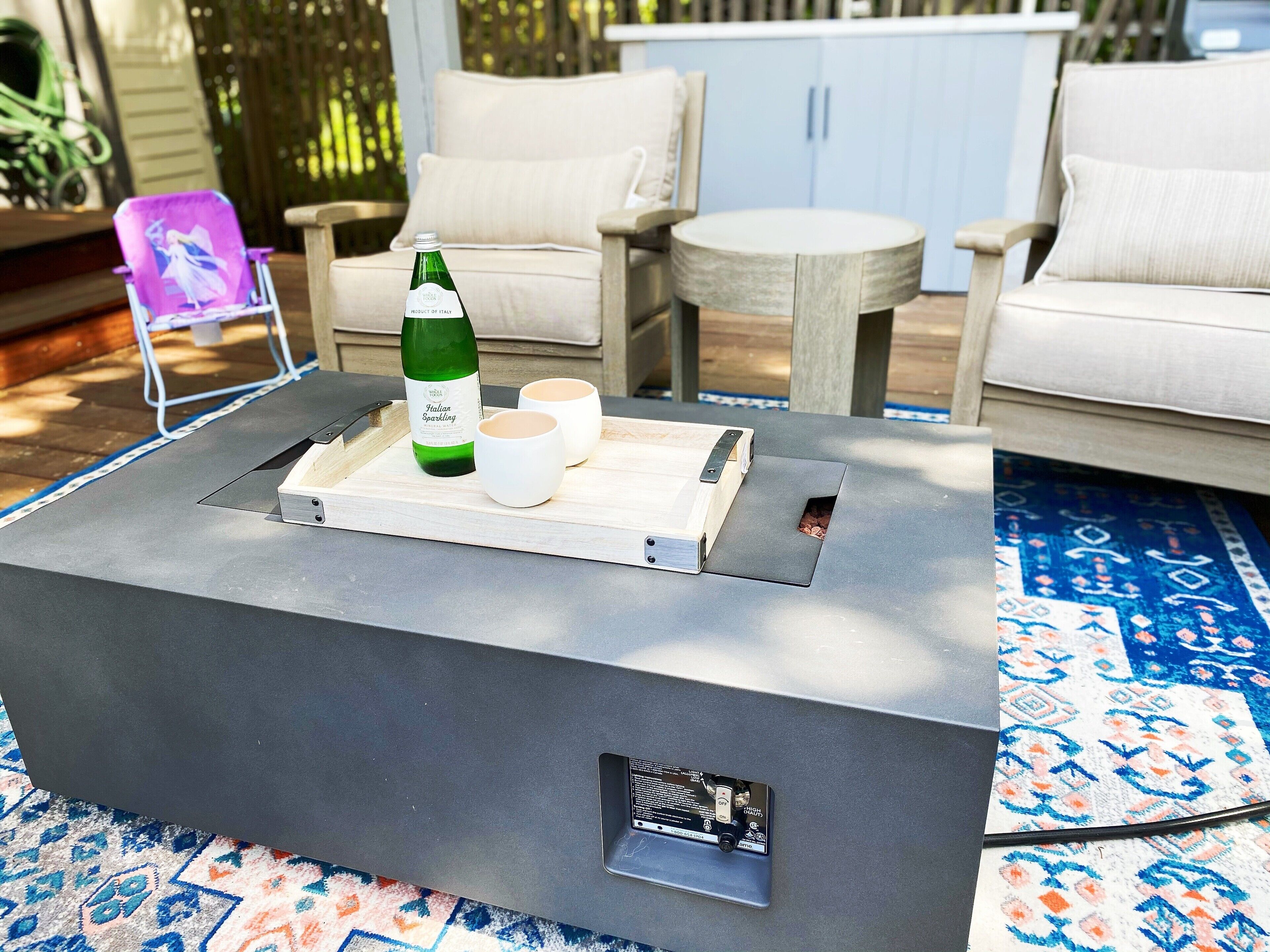 A modern outdoor seating area with a metal table, two white cups, and a green bottle.