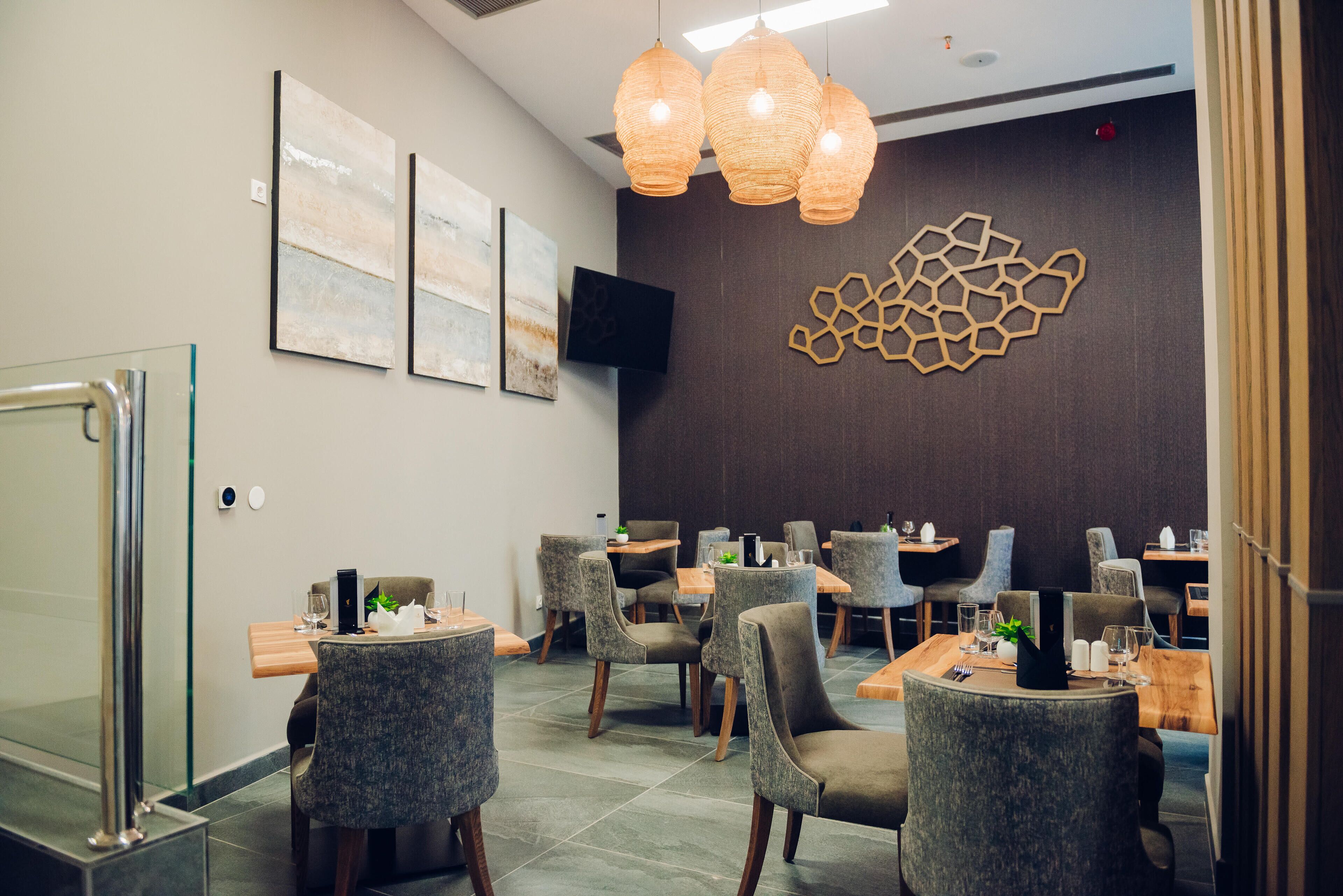 Un restaurante moderno con sillas tapizadas en gris, mesas de madera e iluminación colgante.
