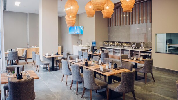 A modern restaurant with multiple dining tables and chairs, a bar area, and hanging wicker pendant lights. - Polana Plaza Hotel (Maputo)