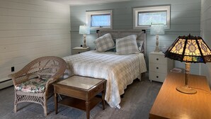 Un dormitorio con una cama, dos mesitas de noche, una silla y una lámpara.
