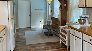 Una cocina con armarios de madera, un refrigerador, una mesa de comedor con sillas y una lámpara colgante.