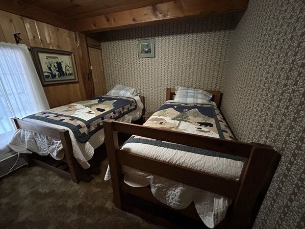 Quarto com duas camas beliches de madeira, papel de parede estampado, um quadro na parede e uma janela com cortinas.