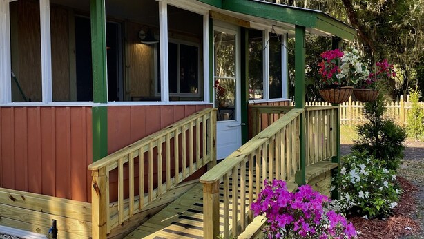 A house with a porch, wooden steps, and a small garden with flowers. - Cottage Americana at Coco Ranch (Ocklawaha)