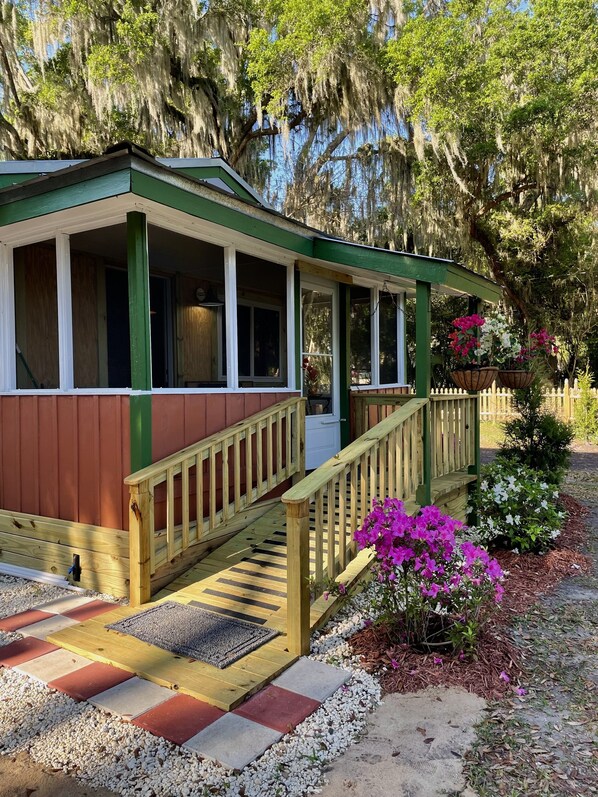Guests can enjoy a sheltered porch with a staircase leading up to the entrance, surrounded by a charming garden with vibrant flowers and a gravel path.