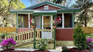 A cabin with a porch, a covered deck, and a small garden with flowers. - Cottage Americana at Coco Ranch (Ocklawaha)