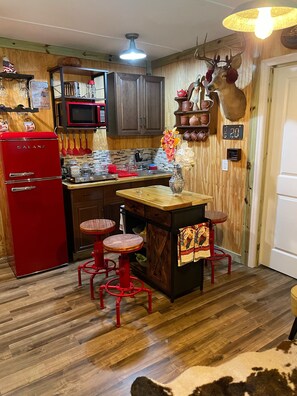 A rustic kitchen with wooden cabinets, a red refrigerator, and a wooden bar counter with stools. - Cottage Americana at Coco Ranch (Ocklawaha)