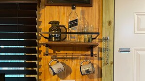A wall with a shelf holding a bottle, a mug, and a glass. Below the shelf, there is a framed poster of a guitar and a violin. - Cottage Americana at Coco Ranch (Ocklawaha)