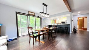 A spacious living area with a dining table, chairs, and a kitchen in the background. - Stratton Mountain Home - Hot Tub, Sauna, Fire Pit, & MORE! (Jamaica)