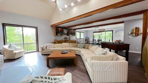 A spacious living area with a large sectional sofa, a coffee table, and a fireplace. There is a balcony with a view of greenery. - Stratton Mountain Home - Hot Tub, Sauna, Fire Pit, & MORE! (Jamaica)