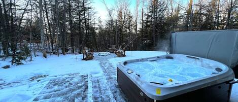 Ein Whirlpool in einer verschneiten Außenanlage mit einem Kiesweg, umgeben von Bäumen.