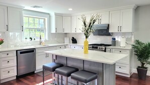 A modern kitchen with white cabinets, a central island with bar stools, a stainless steel dishwasher, and a gas stove.