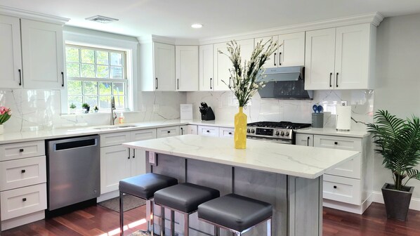 A modern kitchen with white cabinets, a central island with bar stools, a stainless steel dishwasher, and a gas stove.