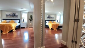 A mirrored view of a bedroom with two beds, wooden flooring, and a large window.