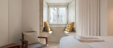 Une chambre d’hôtel avec un lit, deux fauteuils, un petit bureau et une fenêtre avec des rideaux.
