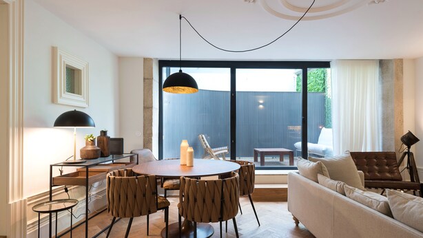 A modern living room with a round dining table, multiple chairs, a sofa, and a large window with a view of greenery. - Classy & Stylish Porto Duplex (Porto)