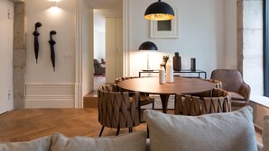 A dining area with a round table, multiple chairs, a pendant light, and a view of a room with a bed and a window. - Classy & Stylish Porto Duplex (Porto)