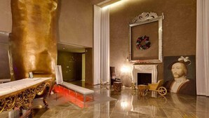 Une chambre luxueuse, ornée d’une grande sculpture dorée, d’une cheminée et d’un tableau de style classique.