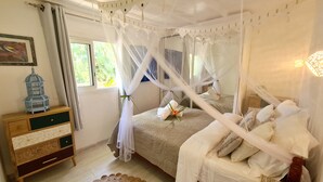 Un dormitorio con cama con dosel, una mesita de noche de madera, una jaula decorativa y vistas a la vegetación.