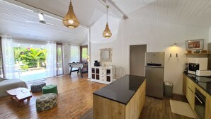 Una cocina moderna con una isla central, un comedor con mesa y sillas, y vistas a un jardín a través de grandes ventanales.