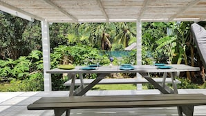 Un área de comedor al aire libre con una pérgola blanca, una mesa de picnic y una mesa dispuesta con platos, vasos y cubiertos.