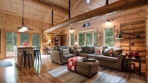 Ein gemütliches Blockhaus-Interieur mit Holzausstattung, einem Essbereich und einer Sitzecke mit Sofa und Hocker.