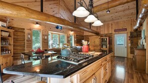 Ein geräumiges Blockhaus-Interieur mit einer großen Kücheninsel, Holzschränken und Blick auf den umliegenden Wald.