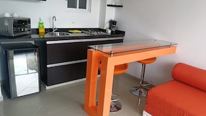 A compact kitchen with a modern design, featuring a built-in microwave, a coffee maker, and a sink. There is a glass table with a metal base and an orange chair. - A spacious and fabulous   387 ft2 studio, near every thing in Cali (Cali)