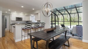 A modern kitchen with white cabinets, a central island with bar stools, and a dining area with a dark wooden table and benches.