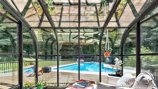 A conservatory with a glass ceiling, a pool, and a seating area with a sofa and ottoman.