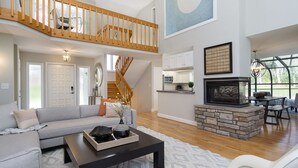 A spacious living room with a gray sofa, a black coffee table, and a fireplace. A staircase leads to an upper level.