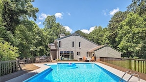 A swimming pool with a house in the background, surrounded by trees.