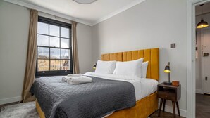 Quarto de hotel com uma cama grande, janela com cortinas, abajur e vista para o exterior.