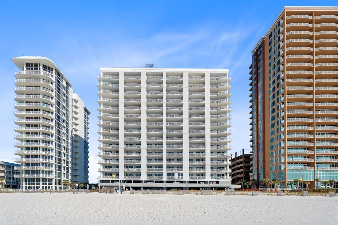 A beachfront hotel with multiple floors, balconies, and a modern architectural design.