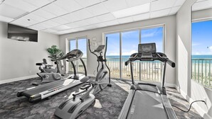 A gym with treadmills, elliptical machines, and a stationary bike, large windows with a beach view. - Beach Front View | Indoor/Outdoor Pools | Hot Tub | Steam Room & Sauna | Sleep 6 (Gulf Shores)