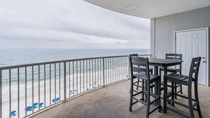 A balcony with a view of the ocean, a table with chairs, and a white door. - Beach Front View | Indoor/Outdoor Pools | Hot Tub | Steam Room & Sauna | Sleep 6 (Gulf Shores)
