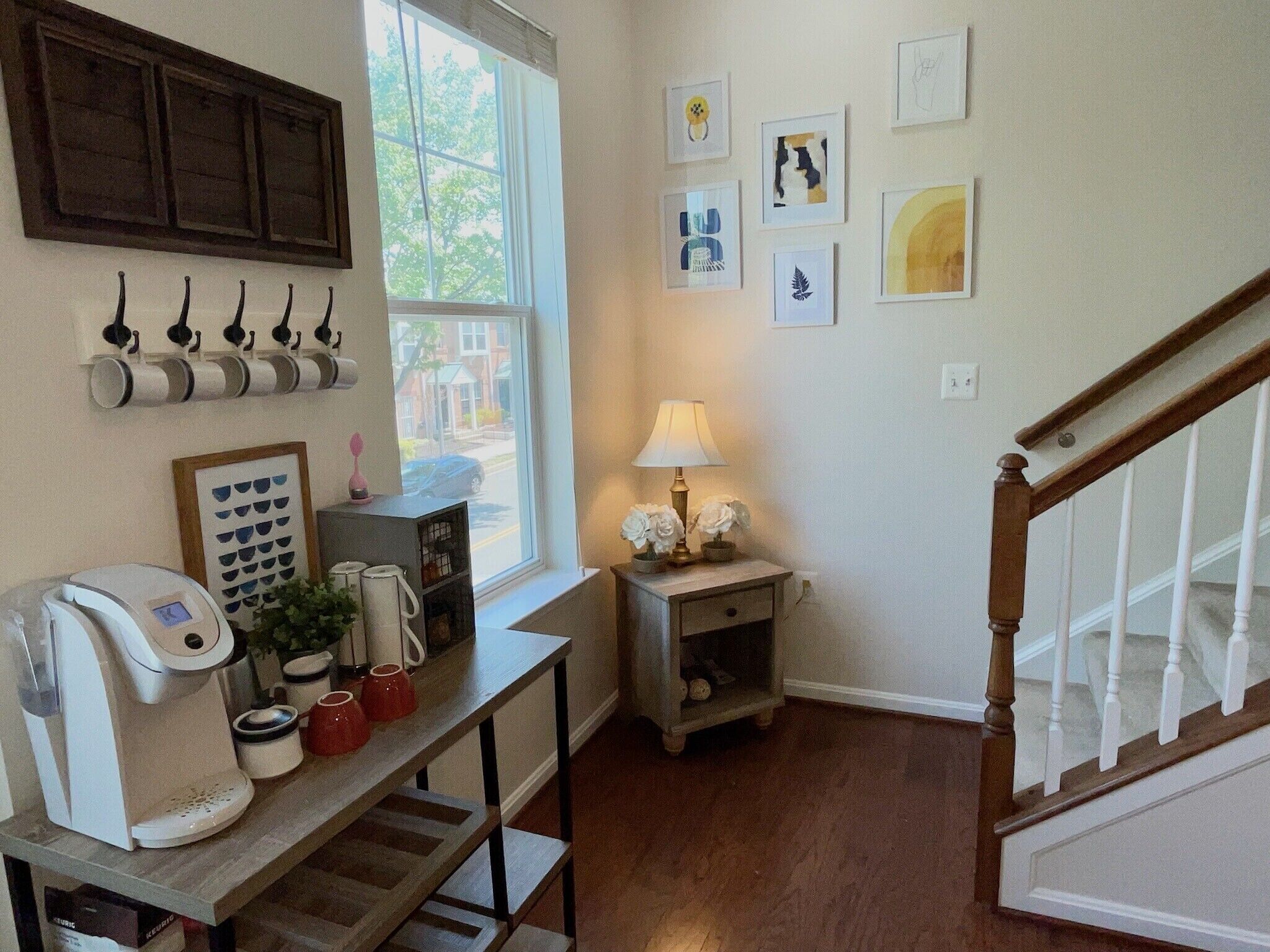 A cozy kitchen with a coffee maker, mugs, and a window with a view of the street.