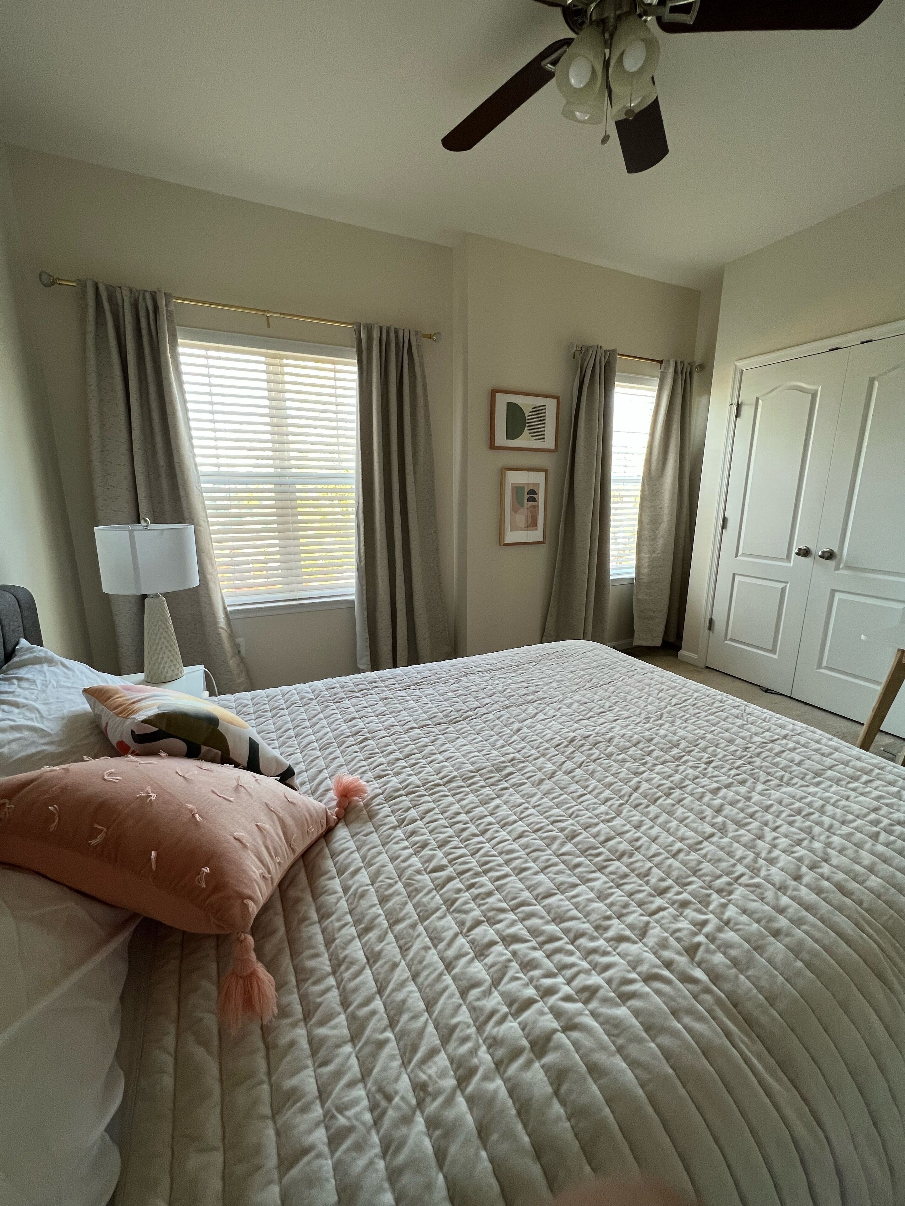 Une chambre à coucher avec un lit, des rideaux, un ventilateur de plafond, une lampe et une armoire.