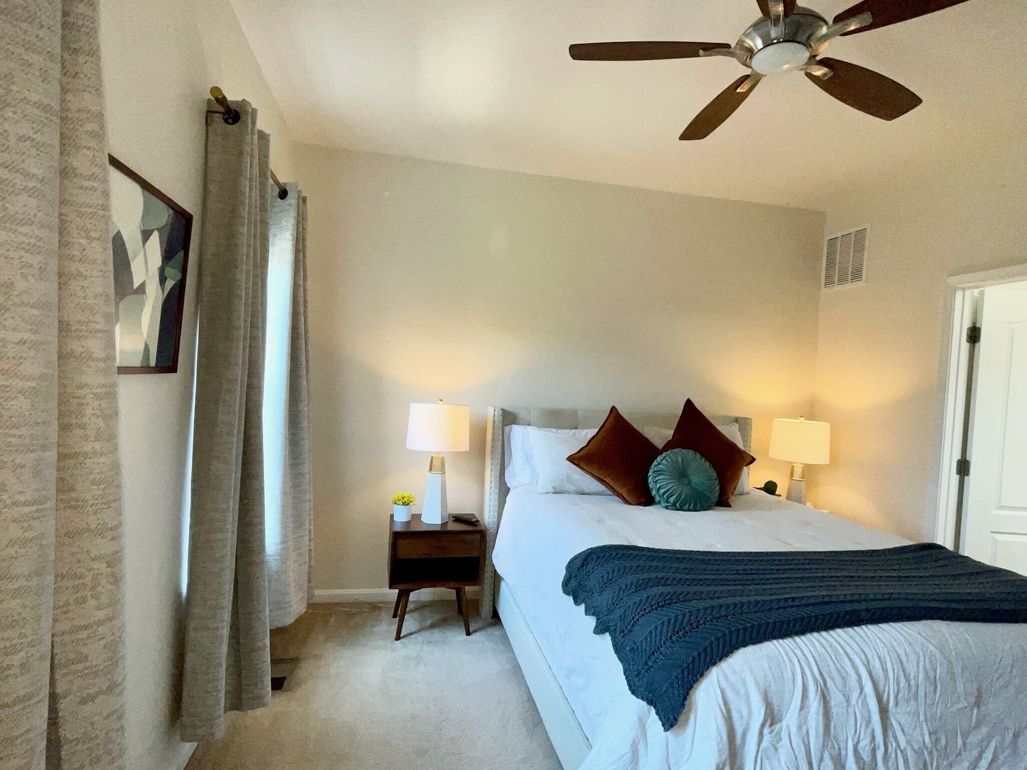 A bedroom with a bed, two bedside tables with lamps, a ceiling fan, and a door.