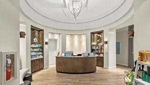 A modern reception area with a central desk, wooden flooring, and a chandelier.