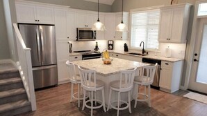 A kitchen with white cabinets, a stainless steel refrigerator, a microwave, and a central island with bar stools. - Steps from the beach and Pool #62 (Osoyoos)