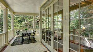 A covered porch with a table and chairs, large glass doors, and a view of a wooded area. - 5 Mi to Old Town Bluffton: Cottage w/ Patio (Bluffton)