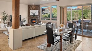 Una sala de estar moderna con chimenea, comedor y ventanas amplias que ofrecen vistas al exterior.