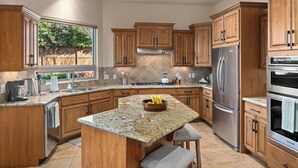 Una cocina con armarios de madera, encimeras de granito, electrodomésticos de acero inoxidable y una isla grande con taburetes.