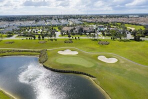Un parcours de golf avec des bunkers, un étang et une zone résidentielle en arrière-plan.