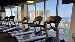 Varias caminadoras en un gimnasio con amplios ventanales que dan a una vista panorámica de la ciudad.